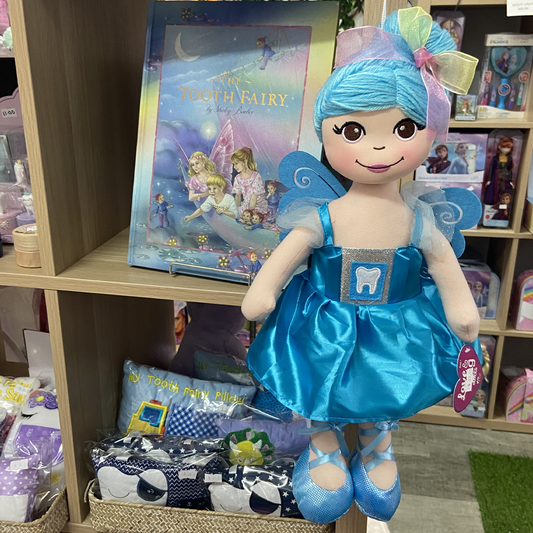 A blue-clad Tooth Fairy doll with a satin dress featuring a tooth emblem, displayed in front of a shelf of various toys.