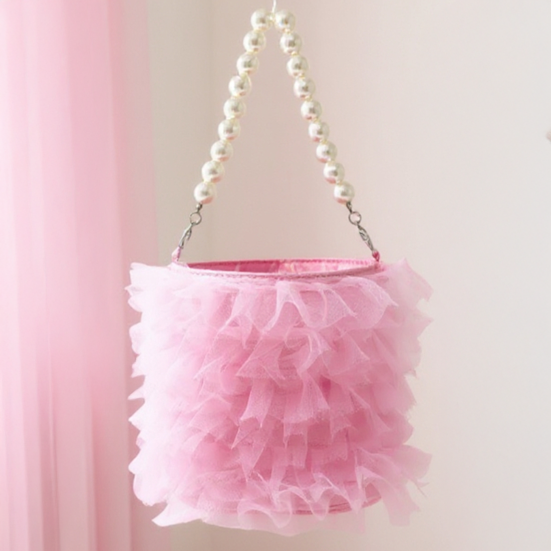 Pink ruffled handbag with pearl handle against a pink background