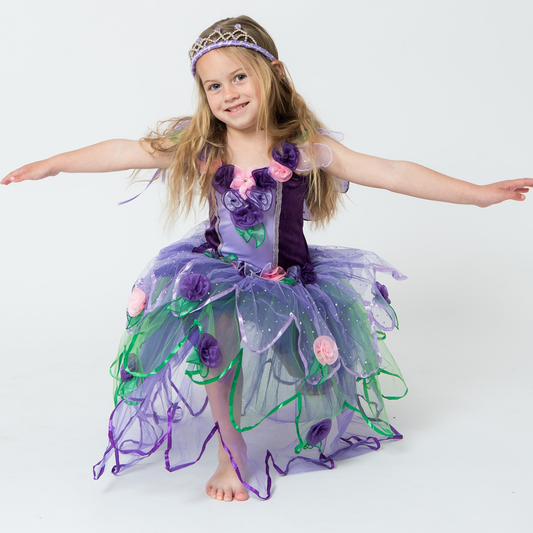 A young girl wearing a purple fairy dress with a full skirt and floral embellishments, complete with sparkling wings on the back bodice.