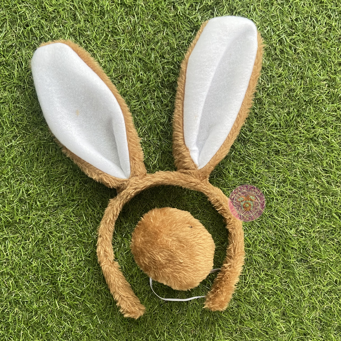 A set of brown bunny ears and tail plush toys laid on green grass.