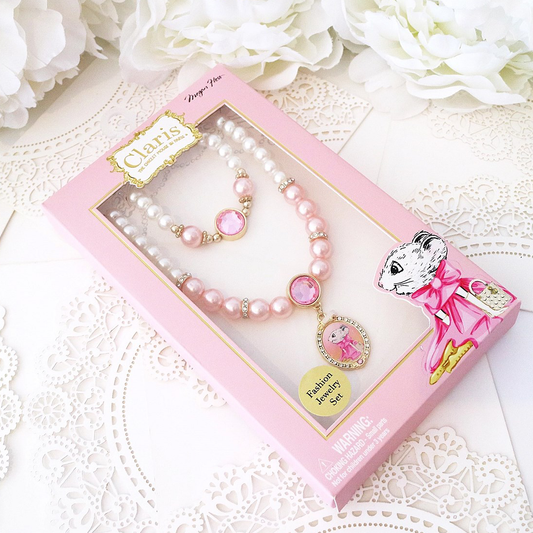 Children's jewelry set with pink dress and accessories in a Claris box on a white lace background.
