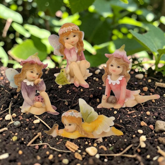 Four small fairy figurines with pastel-colored dresses and wings a with their fairy friends a bird a snail a frog and a lady bug