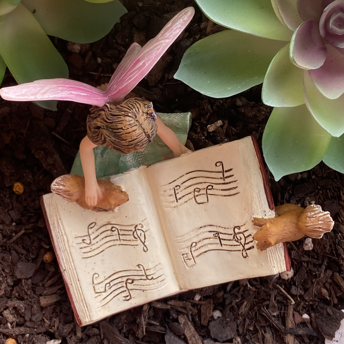 Fairy figurine with bunny ears reading a book of music notes on a garden background