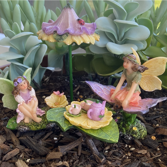 Fairy garden with miniature fairies, flowers, and plants on a natural ground cover.
