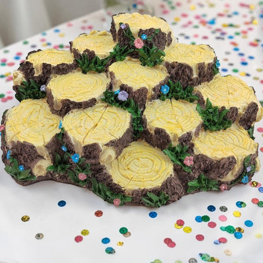 Tree stump cake with yellow icing and brown details on a white surface with colorful sprinkles.