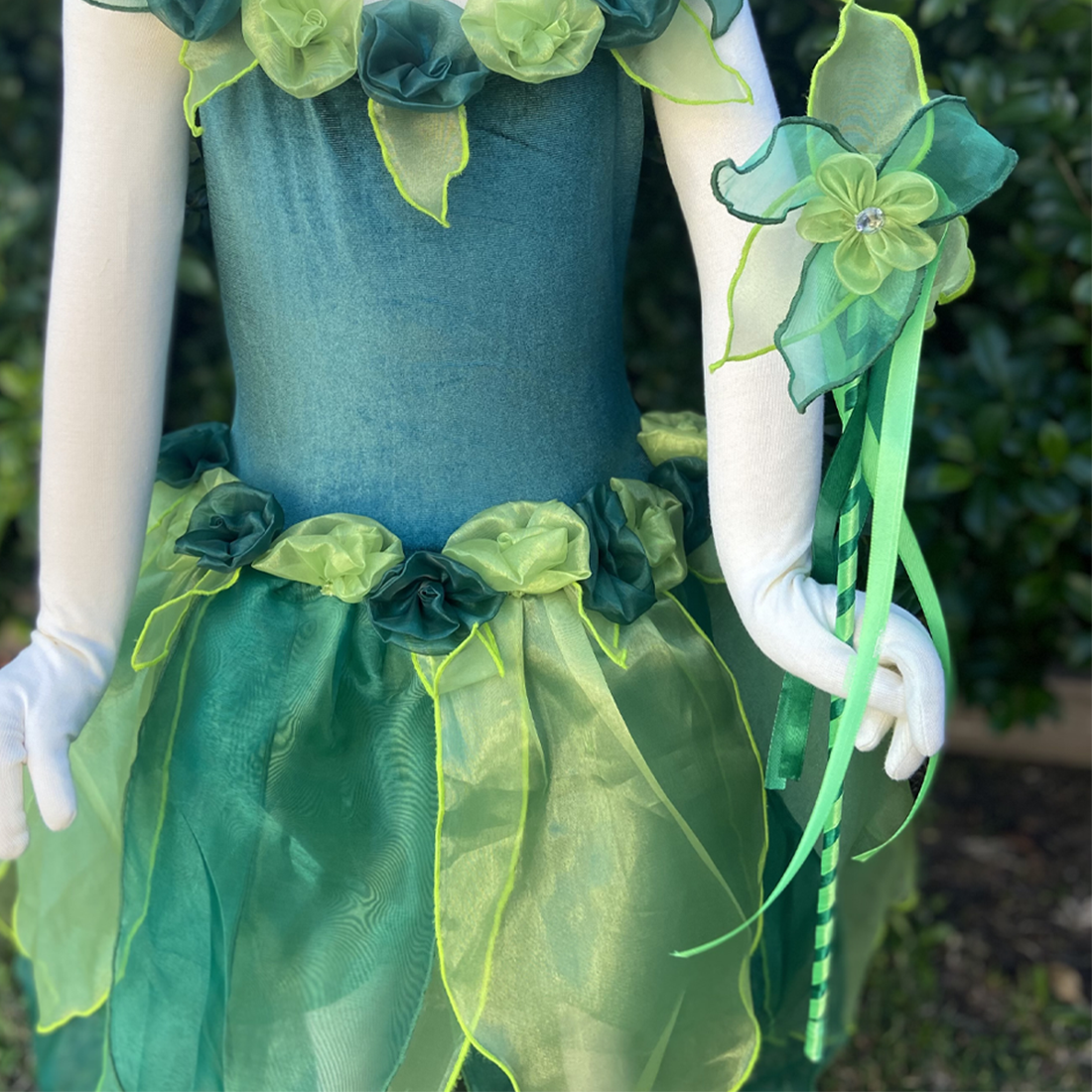 A close-up of a green fairy wand with a handmade flower and diamante detail, and organza petals. The handle is adorned with satin and ribbons.
