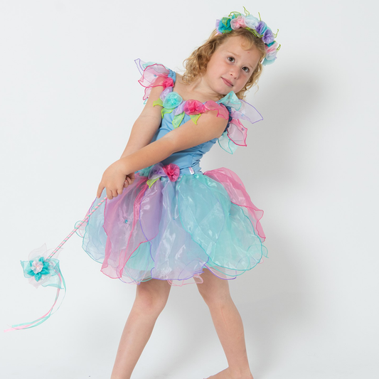 A young girl wearing a blue and multicolored fairy dress with a layered skirt and petalled sleeves, holding a matching wand, with a crown of flowers on her head.