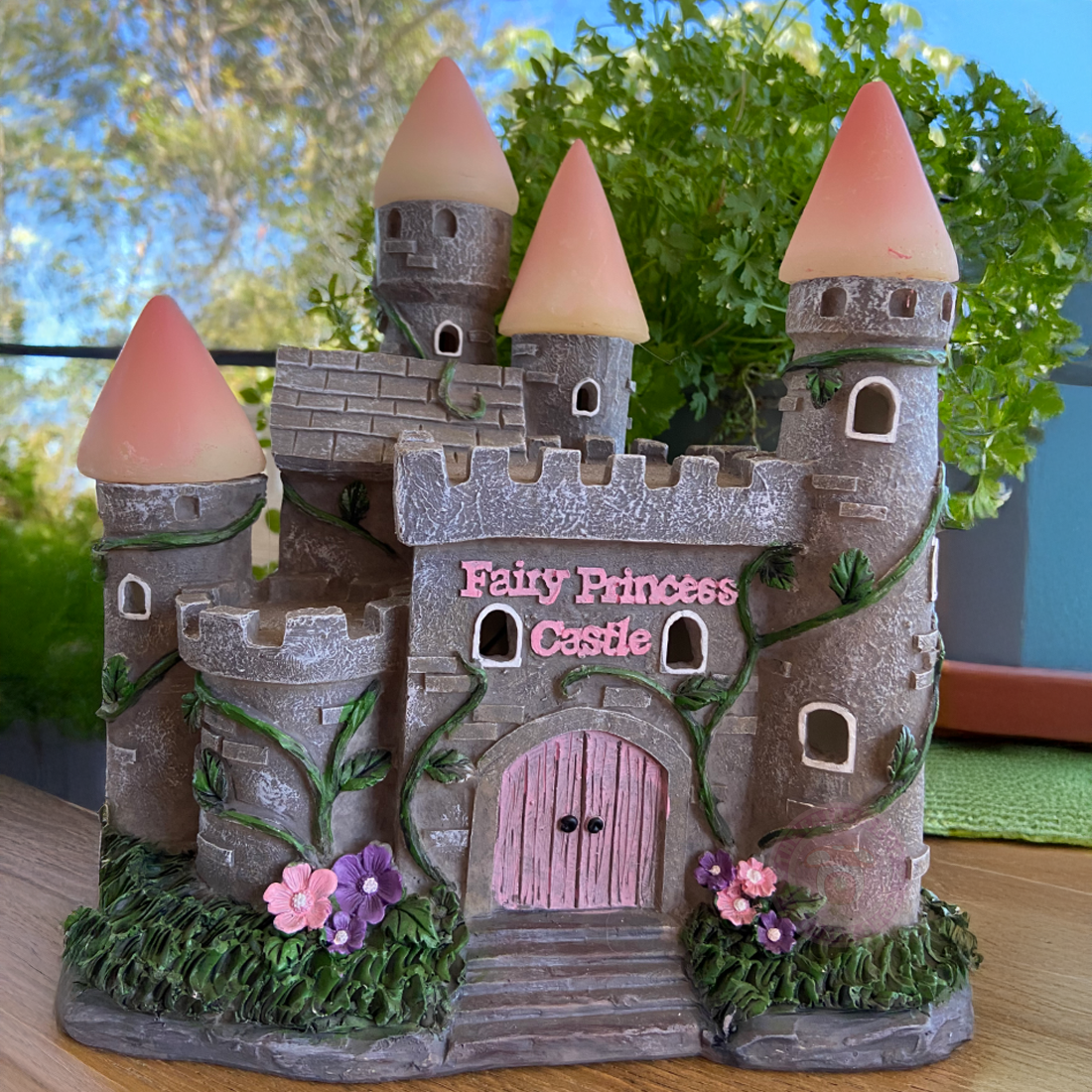 Fairy princess castle toy with pink door and conical towers on a wooden surface.