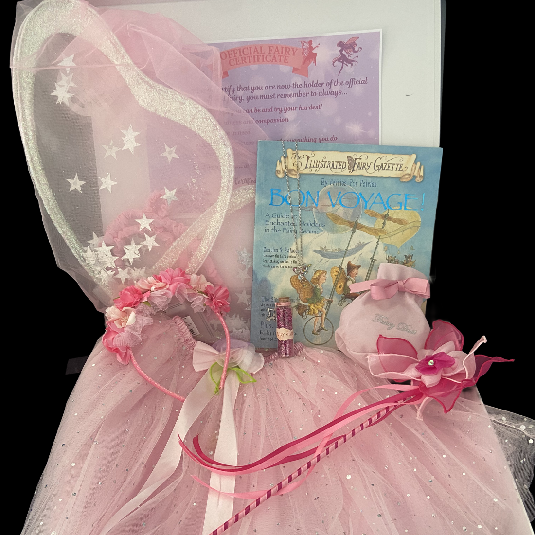 Pink fairy costume with wand, fairy wings, and book titled 'Bon Voyage' on a black background