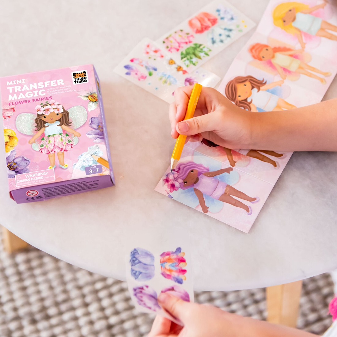 Child using a pencil to color in a fairy-themed coloring book with a 'Minty Transfer Magic' product box.