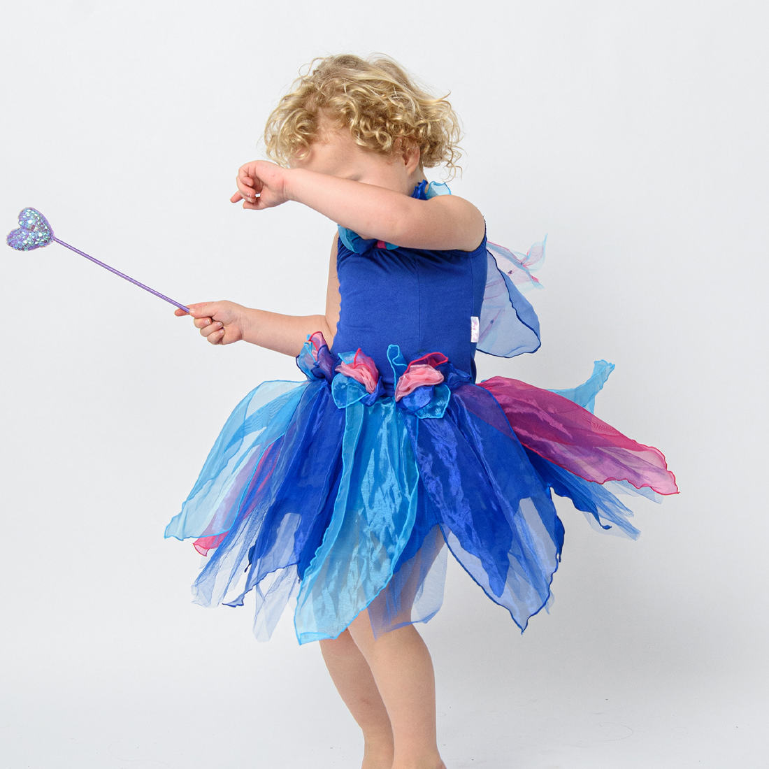 A young child wearing a blue pixie fairy dress with handmade flowers and attached wings, posing with a wand.