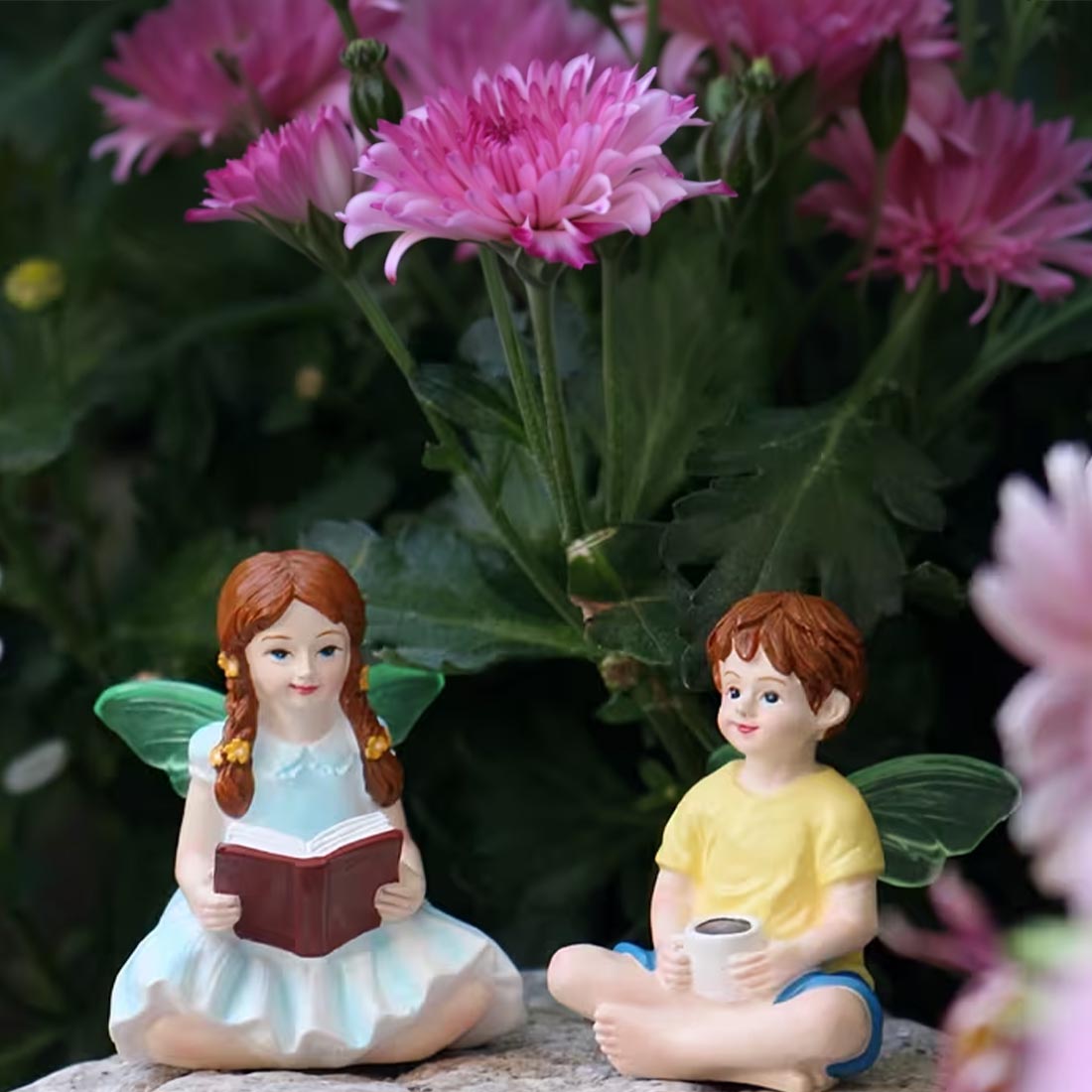 Two fairy figurines, a girl and a boy, sitting among pink flowers.