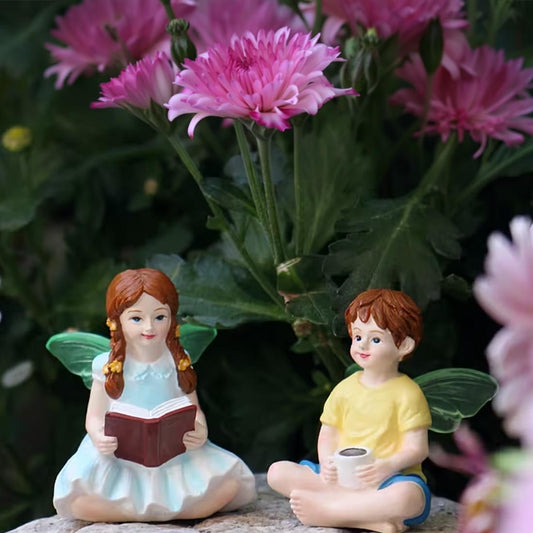 Two fairy figurines, a girl and a boy, sitting among pink flowers.