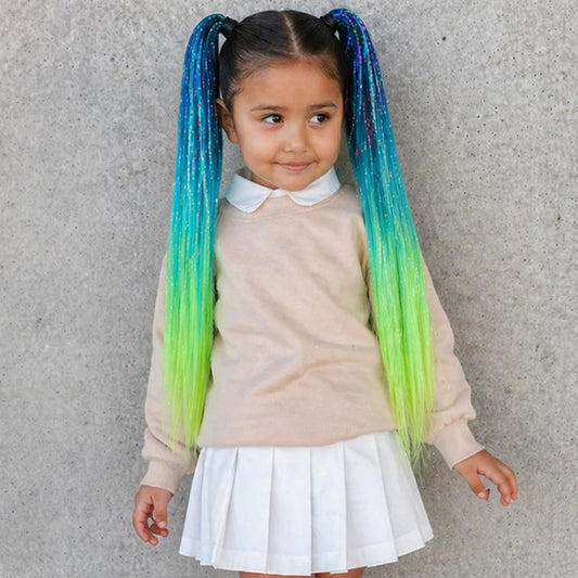 Child with colorful braided hair standing against a concrete wall