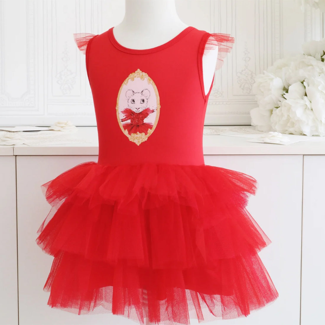 A red sleeveless claris in paris children's fairy dress with a tiered tulle skirt and a claris in paris holiday heist graphic on the front, displayed on a white mannequin torso in a bright indoor setting.