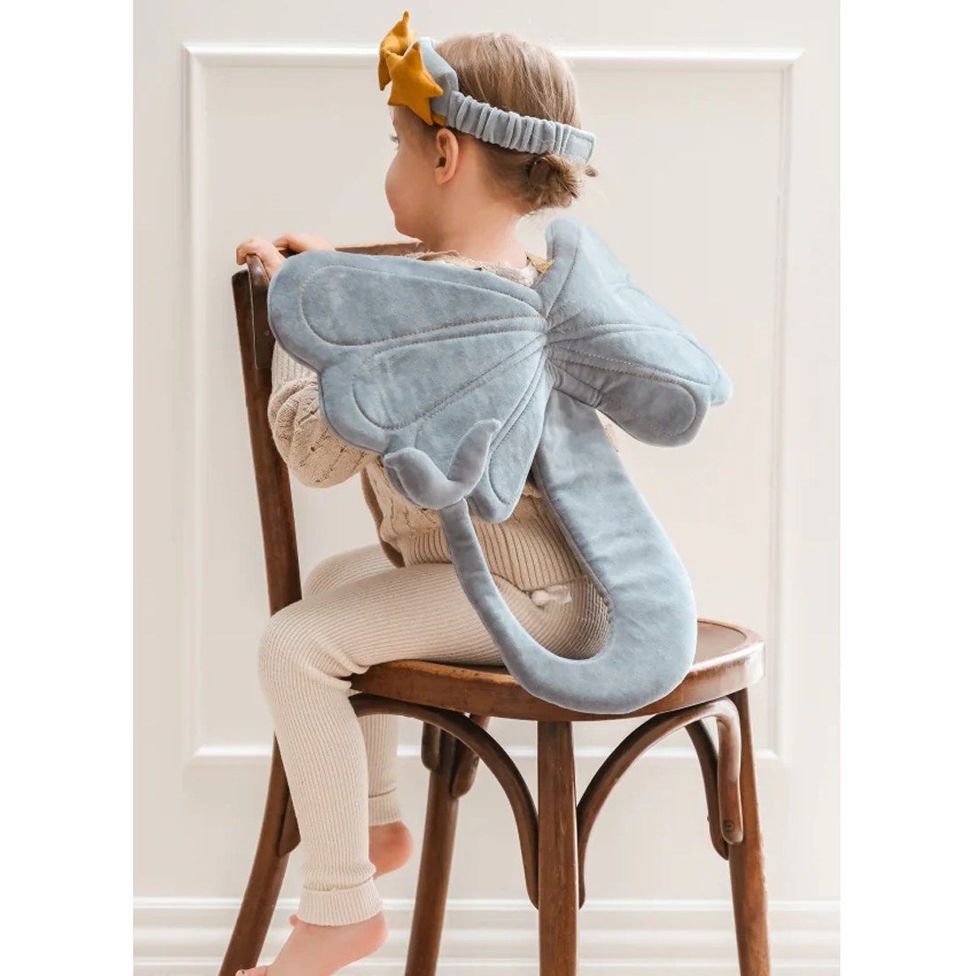 Child sitting on a chair with a large blue dragon toy draped over their shoulders.