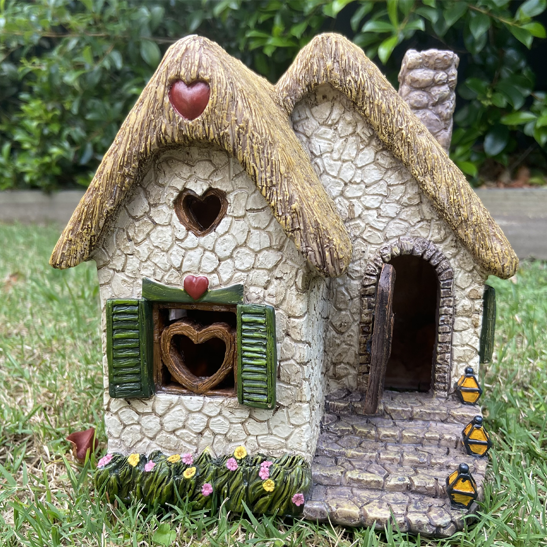 Small stone cottage with thatched roof and heart details on a grassy background