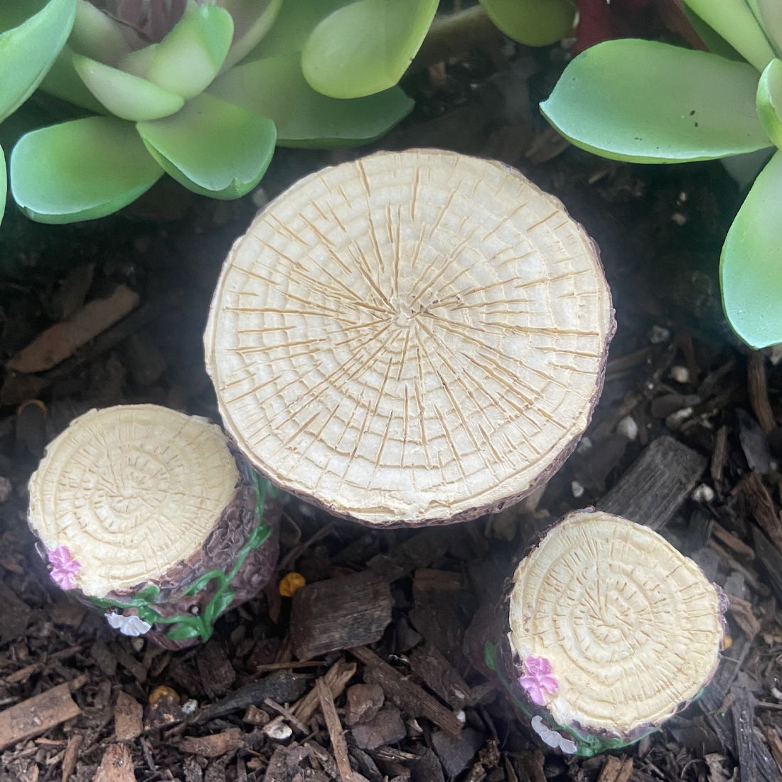 Three decorative mushroom logs with floral bases on a natural ground cover