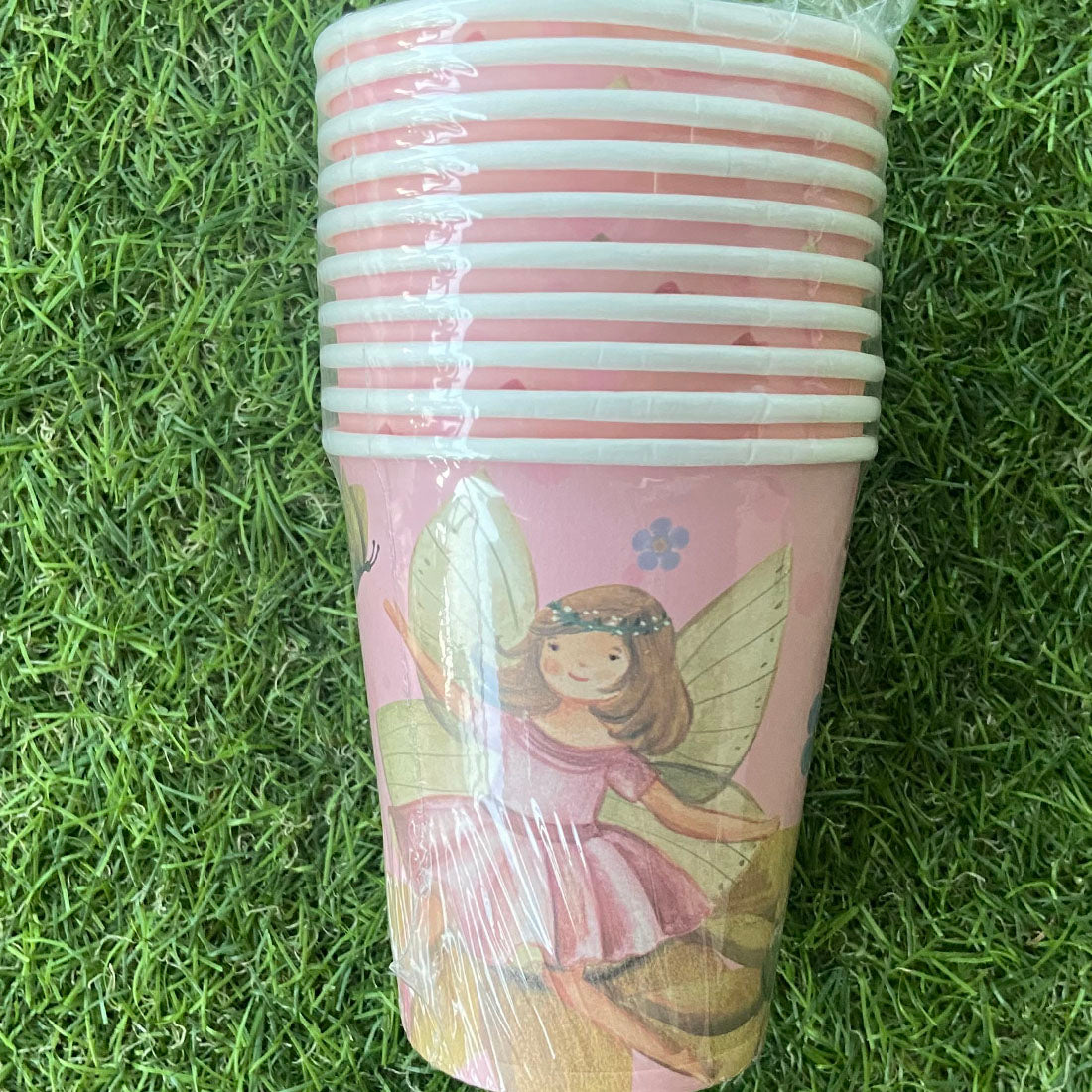 Stack of pink paper cups with fairy design on grass