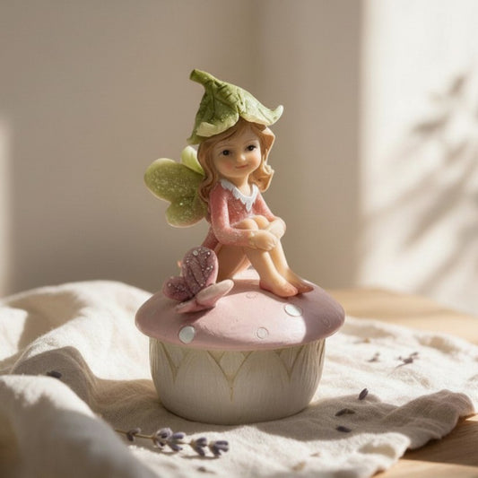A fairy trinket box featuring a hand-painted fairy sitting on top of a box in  the shape of a mushroom with a pink lid