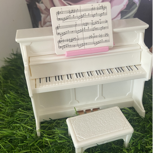 Miniature white piano for dolls house.  The set includes a piano with a closable keyboard cover, a stool, and a sheet of music.