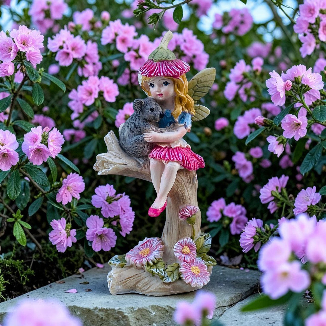 Statue of a fairy holding a koala surrounded by pink flowers