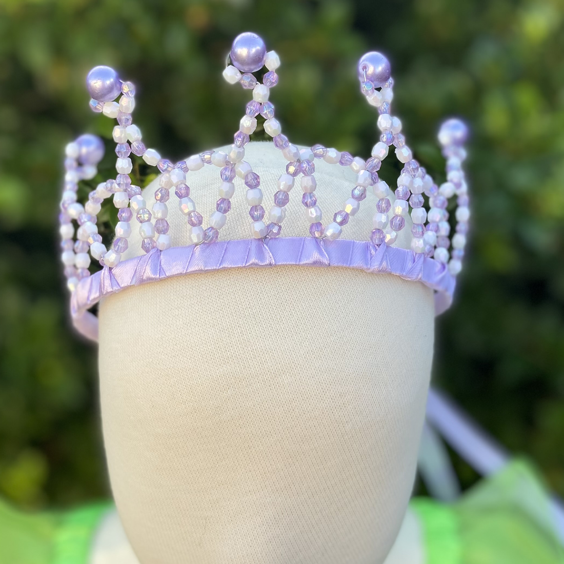 A purple princess tiara crown with bead embellishments displayed on a mannequin head.