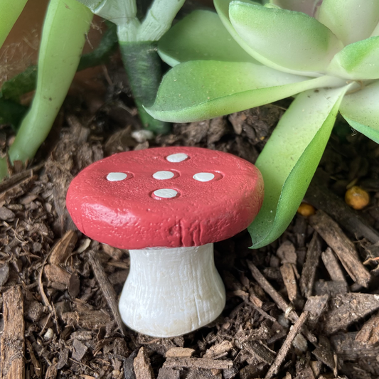 Red and white mushroom figurine on soil with green plants