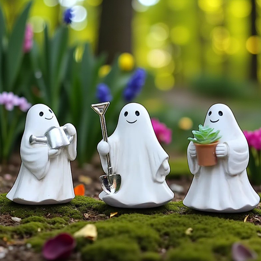 Three white ghost figurines with gardening tools and a plant on a green surface with blurred floral background