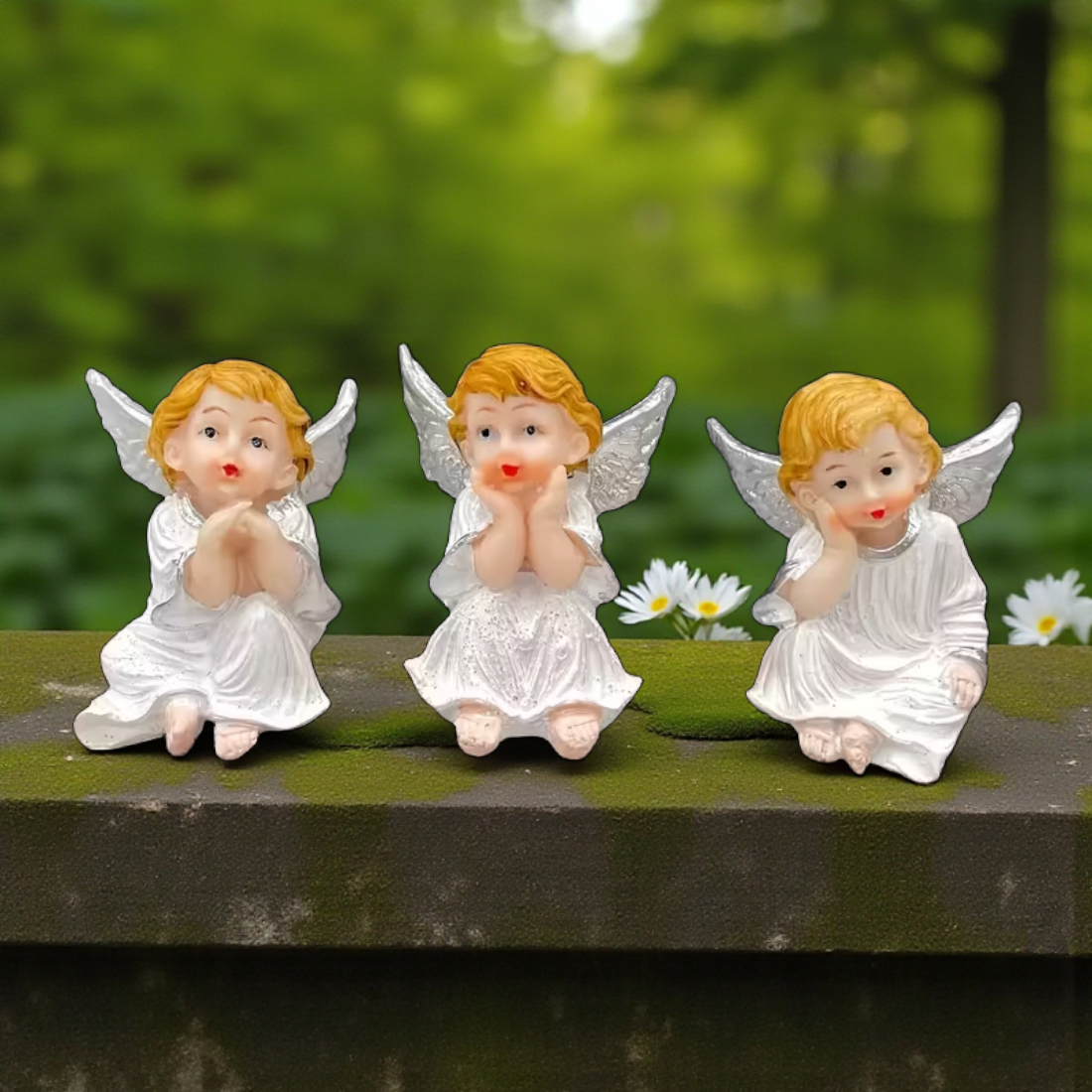 Three angel figurines with wings on a green surface with a blurred natural background
