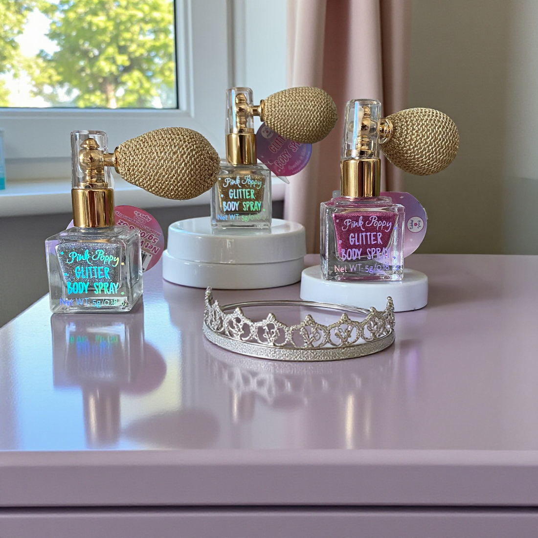 Three bottles of 'Pink Poppy Glitter Body Spray' on a surface with a decorative tiara in front.