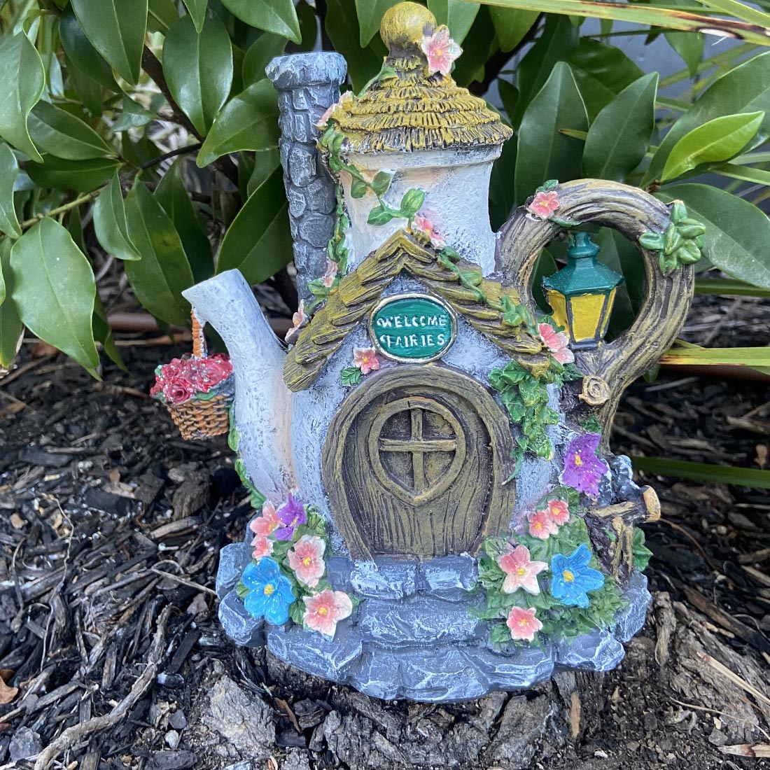 Fairy house made from a teapot with flowers and a door, set against a natural background.