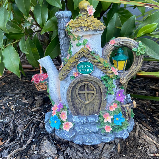 Fairy house made from a teapot with flowers and a door, set against a natural background.